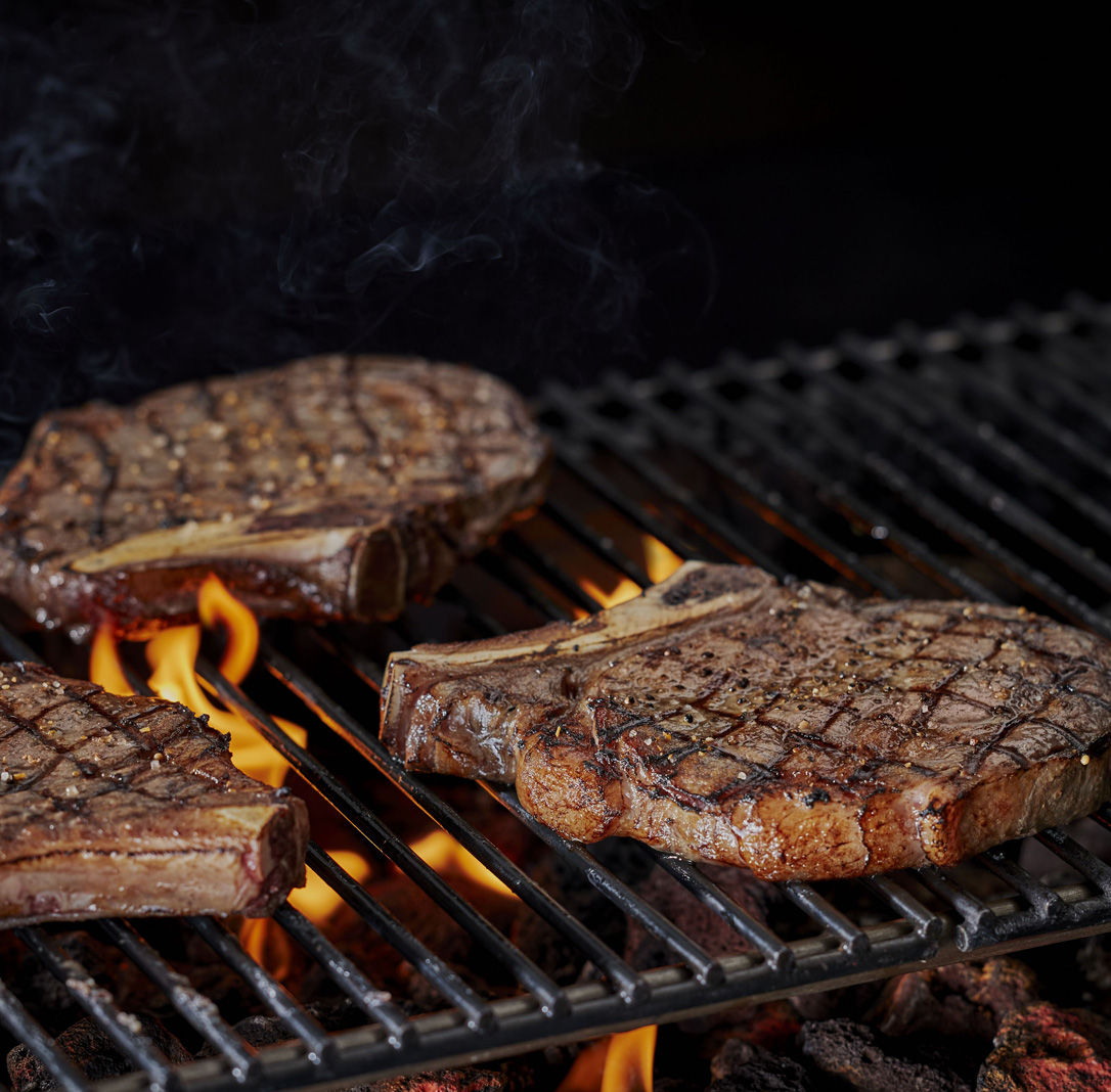 Grilled steaks sizzling over an open flame on a barbecue grill.