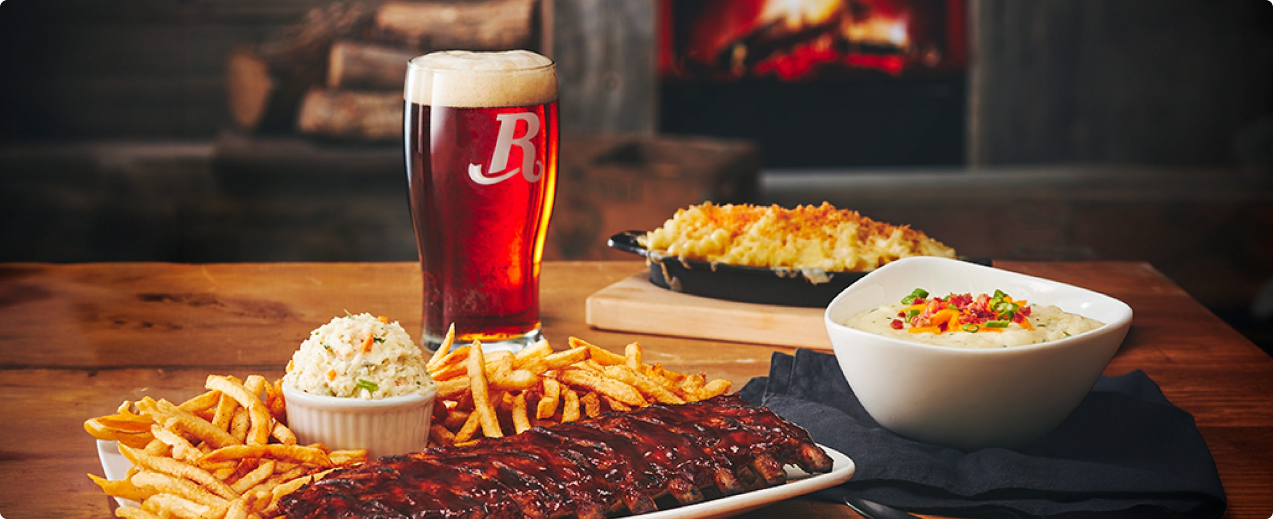 Delicious ribs, fries, coleslaw, beer, and creamy sides on a rustic table setting.