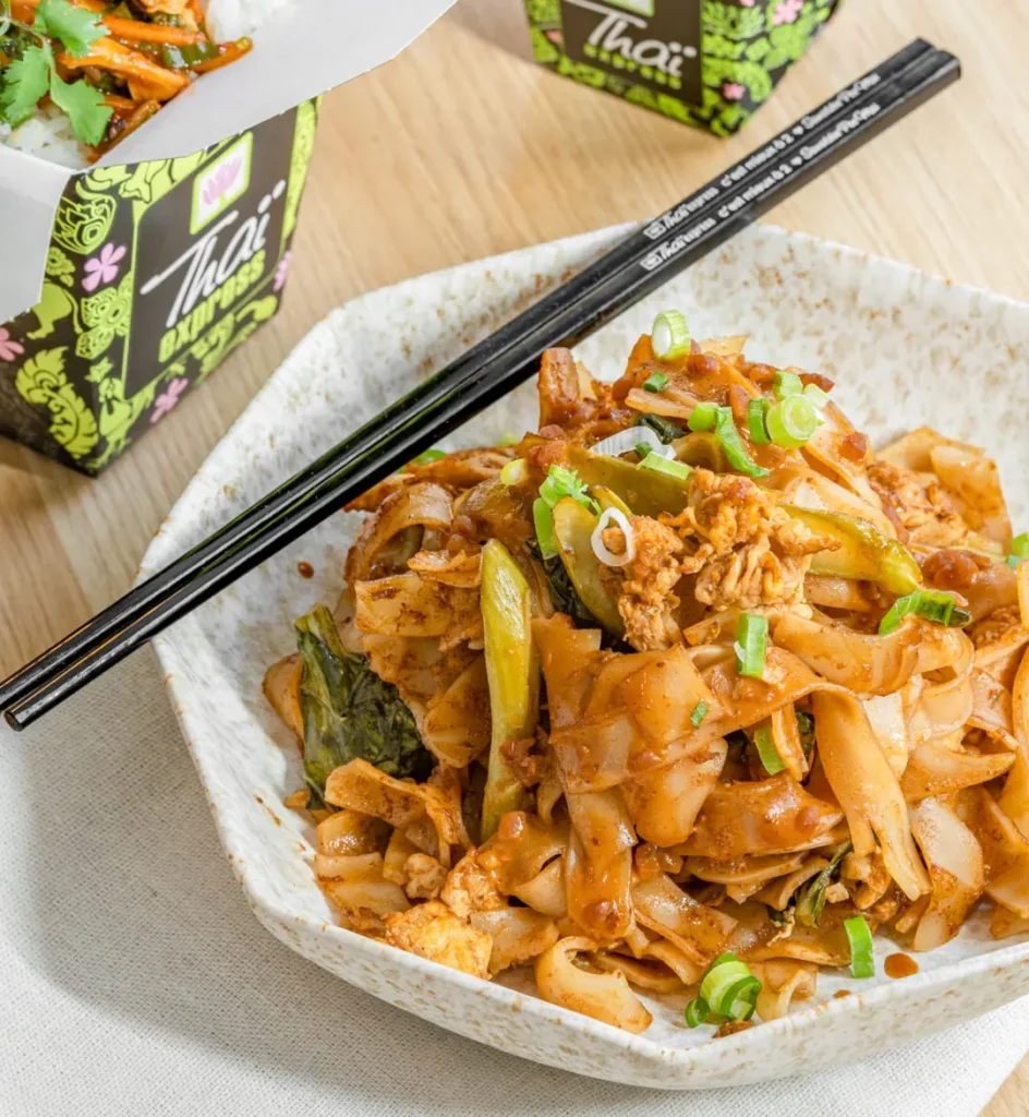 A delicious plate of Pad See Ew Thaï Express noodles, topped with chicken, vegetables, and fresh green onions.