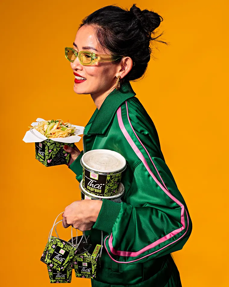 Smiling woman in stylish green attire holding a Thaï Express takeout box, showcasing the vibrant and modern appeal of the brand